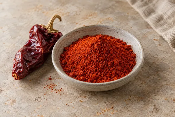 Geräuchertes Paprikapulver in einer Keramikschale neben einer getrockneten Paprika